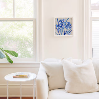 a cozy living room with a white sofa, a small round table, and a framed artwork of blue flowers hanging on the wall.