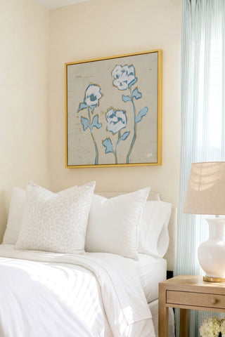 a serene bedroom scene with a bed adorned with white linens and a framed floral artwork hanging above it.