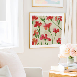 a cozy living room with a white sofa, a framed painting of red flowers on the wall, and a vase of pink flowers on a wooden table.