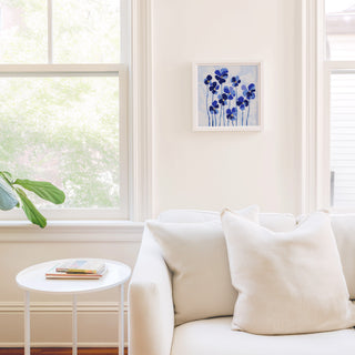 a cozy living room with a white sofa, a small round table, and a framed artwork of blue flowers on the wall.