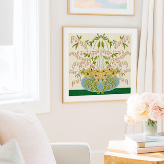 a cozy living room with a framed floral print hanging on the wall, a vase of pink flowers on a table, and a stack of books on a nearby surface.