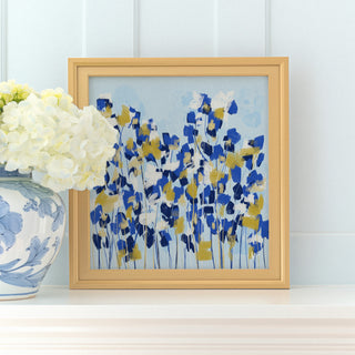 a framed painting of blue and yellow flowers on a white shelf, with a vase of white hydrangeas placed next to it.