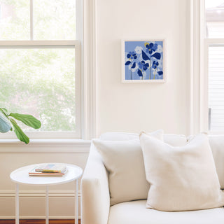 a cozy living room with a white sofa, a small round table, and a framed artwork of blue flowers on the wall.