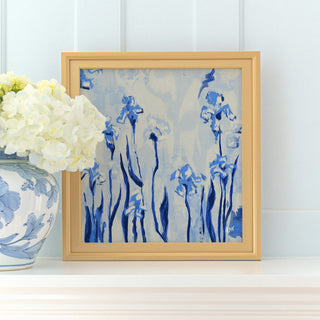 a framed painting of blue flowers on a white shelf, with a vase of white hydrangeas placed next to it.