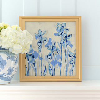 a framed painting of blue flowers on a white shelf, with a vase of white hydrangeas placed next to it.