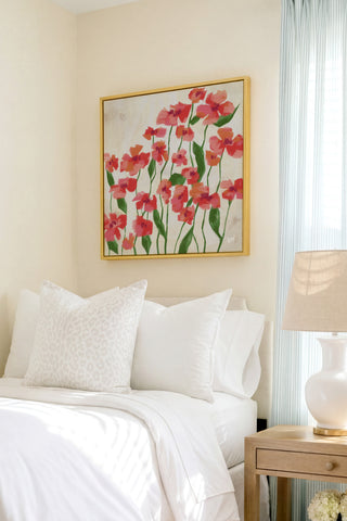 a cozy bedroom with a large bed adorned with white pillows and a white comforter. Above the bed, a framed painting of red flowers hangs on the wall, adding a touch of color and life to the room. To the right of the bed, there is a wooden nightstand with a lamp, providing both functionality and style to the space.