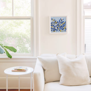 a cozy living room with a white sofa, a small round table, and a framed artwork of blue and yellow flowers on the wall.