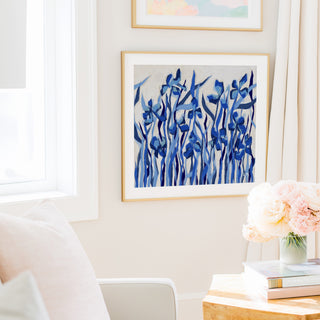 a cozy living room with a white sofa, a framed artwork of blue flowers on the wall, and a vase of pink flowers on a wooden table.