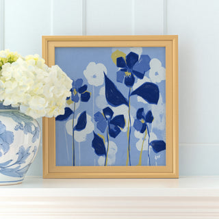 a framed painting of blue flowers on a white shelf, with a vase of white hydrangeas placed next to it.