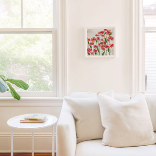 a cozy living room with a white sofa, a small round table, and a framed artwork of red flowers on the wall.