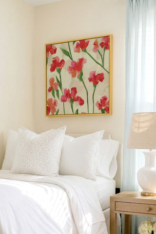 a cozy bedroom with a bed adorned with white pillows and a floral print bedspread. Above the bed, a framed painting of red flowers hangs on the wall, adding a touch of color and life to the room.