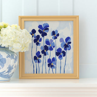 a framed painting of blue flowers on a white background, placed on a shelf next to a vase of white hydrangeas.