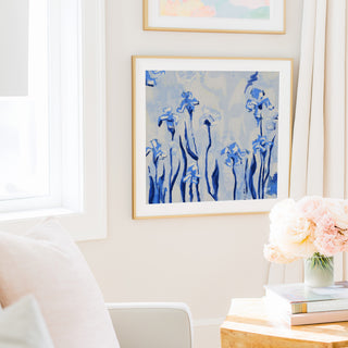 a cozy living room with a white sofa, a framed painting of blue flowers on the wall, and a vase of pink flowers on a wooden table.