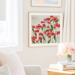 a cozy living room with a framed painting of red flowers hanging on the wall, a vase of pink flowers on a table, and a bookshelf filled with books.
