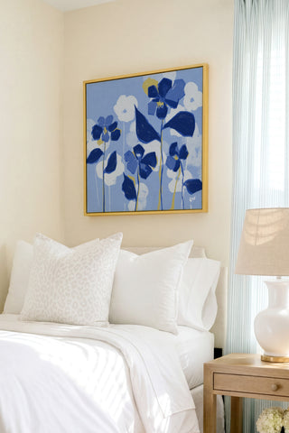a bedroom with a bed, a nightstand, and a framed artwork featuring blue flowers on the wall.
