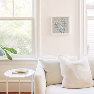 a cozy living room with a white sofa, a small round table, and a framed artwork of flowers on the wall.