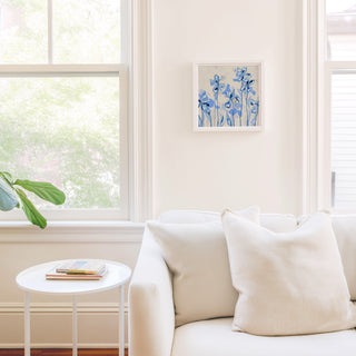 a cozy living room with a white sofa, a small round table, and a framed artwork of blue flowers on the wall.