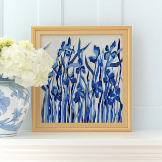 a framed painting of blue flowers on a white background, placed on a shelf next to a vase of white hydrangeas.