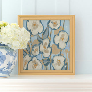 a framed painting of white flowers with blue and green accents, placed on a white shelf next to a blue and white vase with white flowers.