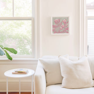 a cozy living room with a white sofa, a small round table, and a framed picture of pink flowers on the wall.