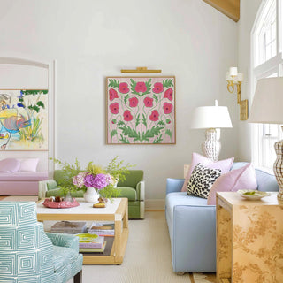 a bright and colorful living room with a floral-patterned painting on the wall, a green sofa, a blue armchair, and a wooden coffee table with a vase of flowers.