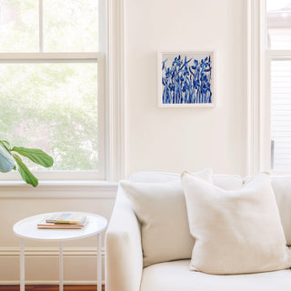 a cozy living room with a white sofa, a small round table, and a framed blue abstract painting hanging on the wall.