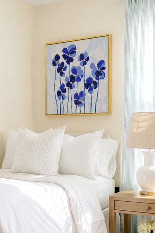 a serene bedroom scene with a bed adorned with white linens and a framed painting of blue flowers hanging above it.