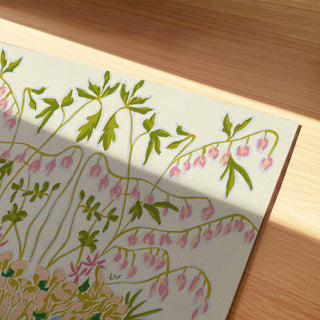 a painting of a plant with pink flowers and green leaves, placed on a wooden surface.