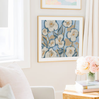 a cozy living room with a white sofa, a framed artwork of white flowers on the wall, and a vase of pink flowers on a wooden table.