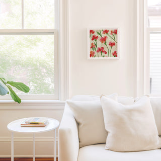 a cozy living room with a white sofa, a small round table, and a framed picture of red flowers on the wall.